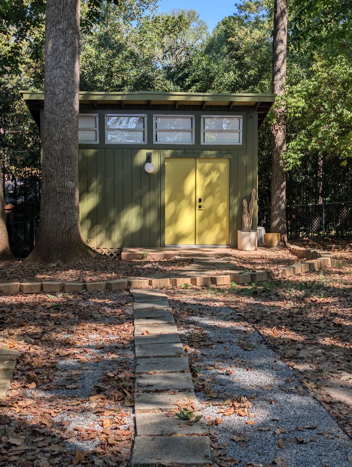 A mid-century style outbuilding in the backyard with clerestory windows, olive siding and yellow double doors, reached by a stone path